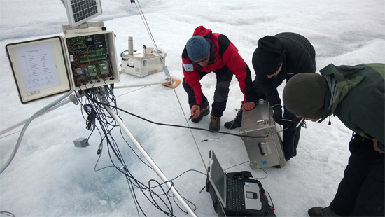 photo of three researchers working on ice monitoring equipment on a glacier