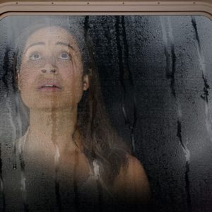 photo of woman looking through rain-splattered window